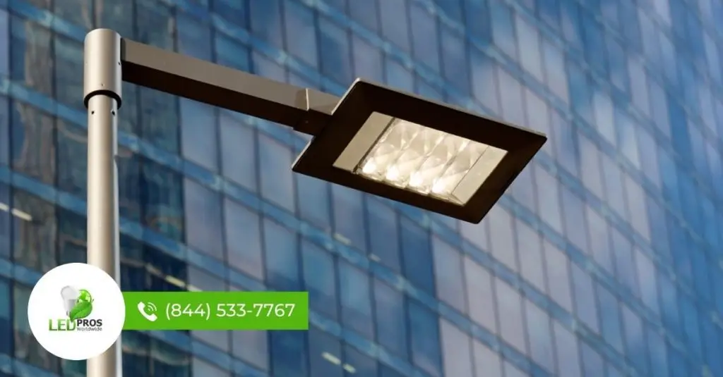 LED street light fixture mounted on a metal pole in front of a commercial glass building, providing energy-efficient roadway and perimeter illumination.